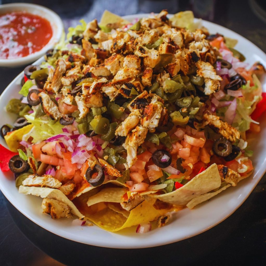 nachos with chicken, tomato, jalapenos, olives, onion, and chips on a white plate